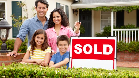 Hispanic family standing outside home smiling with sold sign