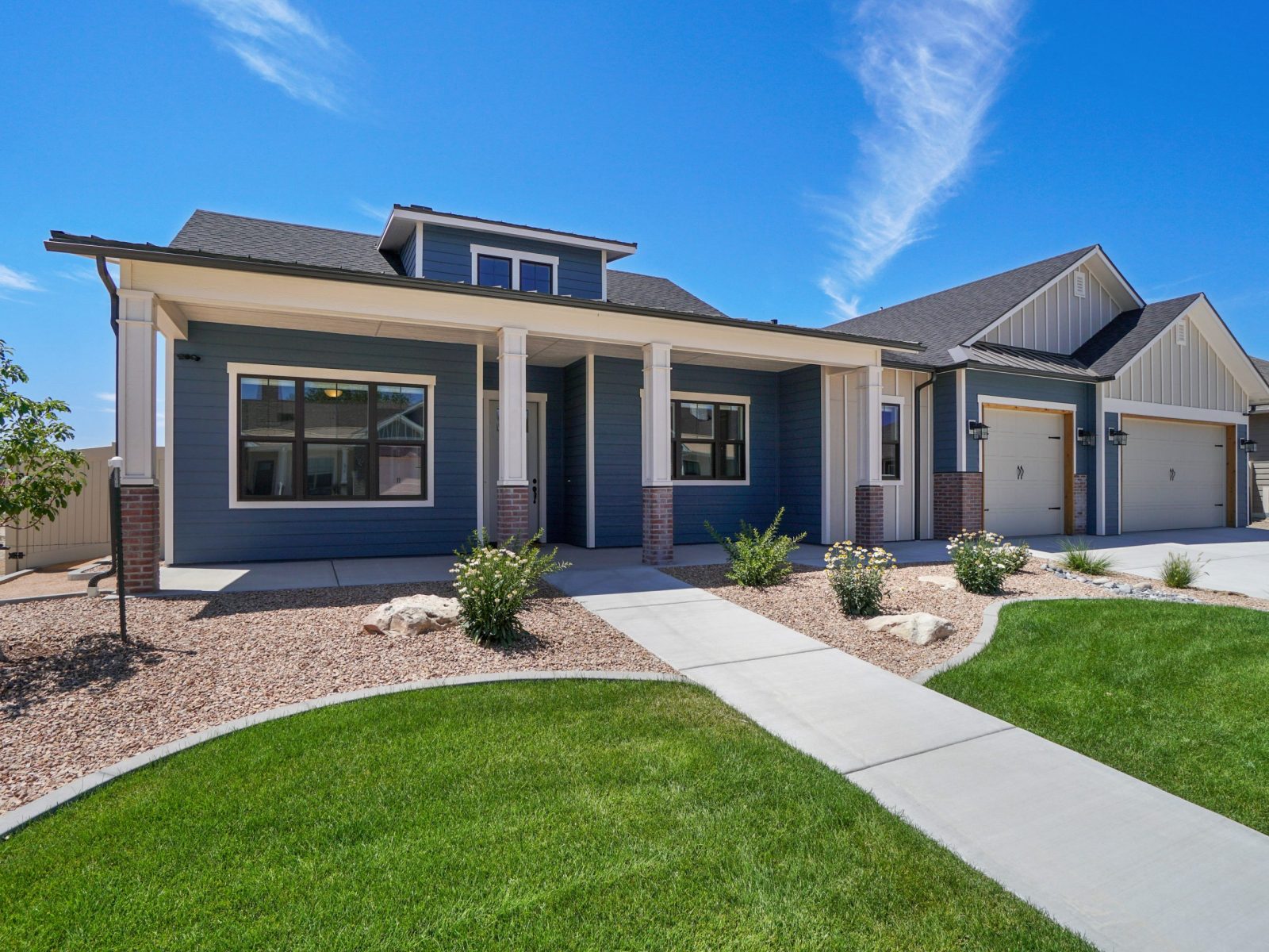 modern landscaped new construction home with blue sky and puffy white clouds. Covered front porch with three car garage